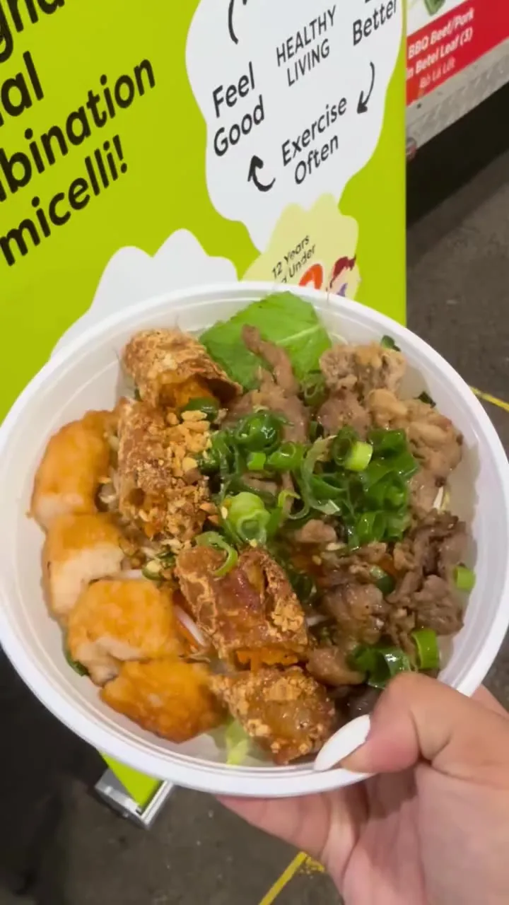 A combination vermicelli bowl with spring rolls, grilled pork, peanuts and spring onion, held up at the truck at the markets